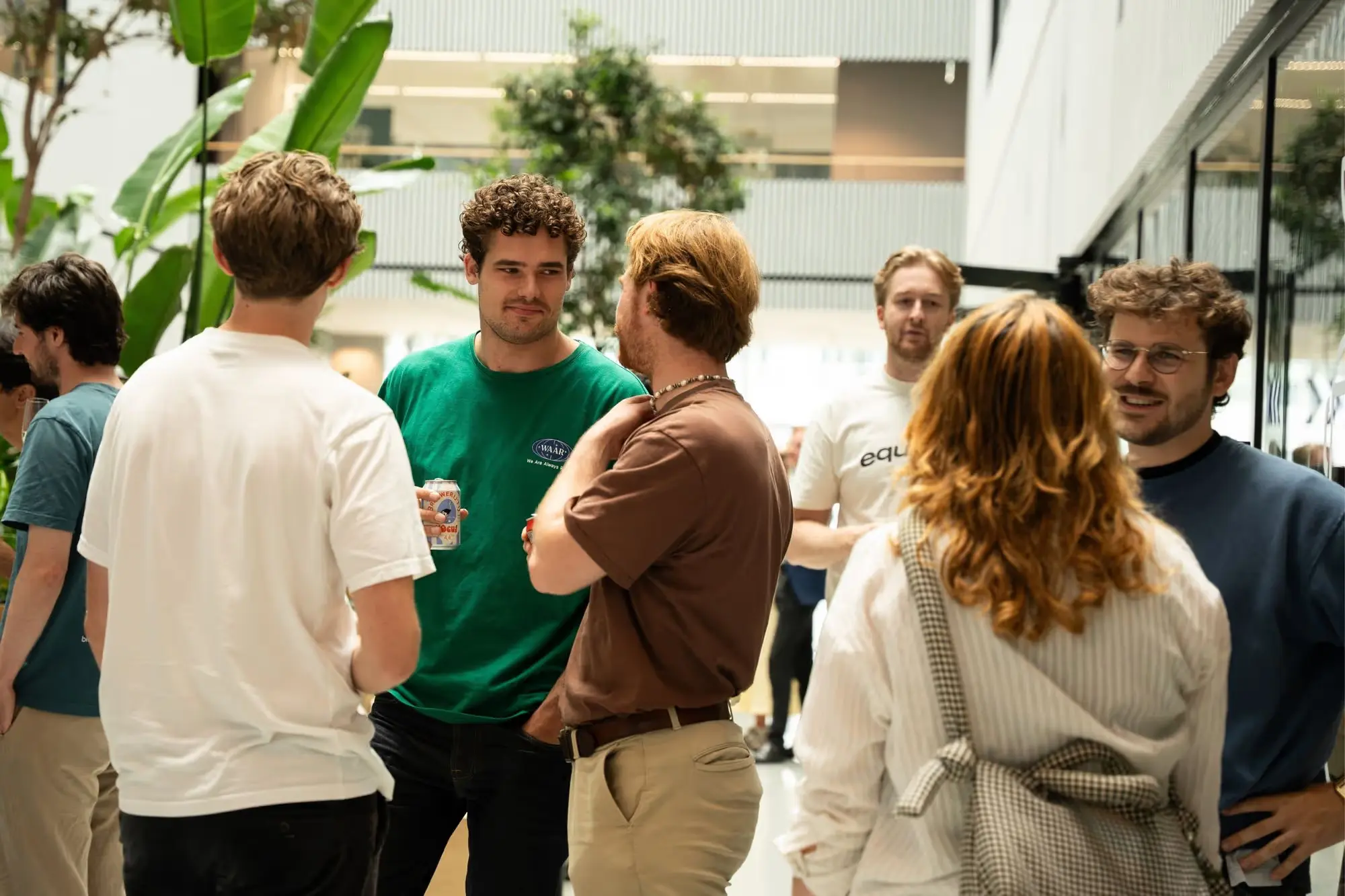 A group of people having drinks together in a light and bright office space with plants, they look happy.