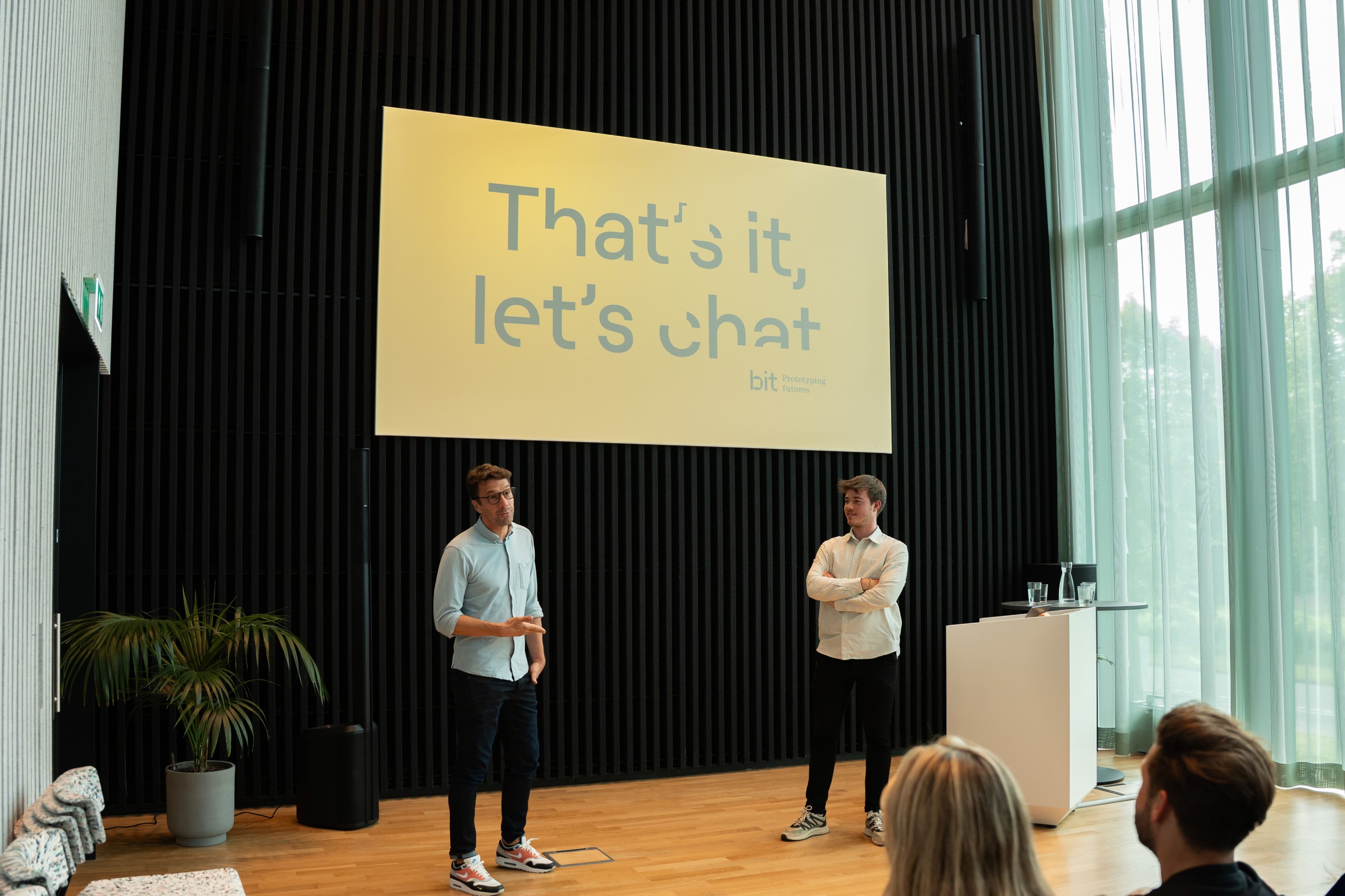 A man standing next to a beamer screen with the text that's it let's chat surrounded by a colleagues listening to him.